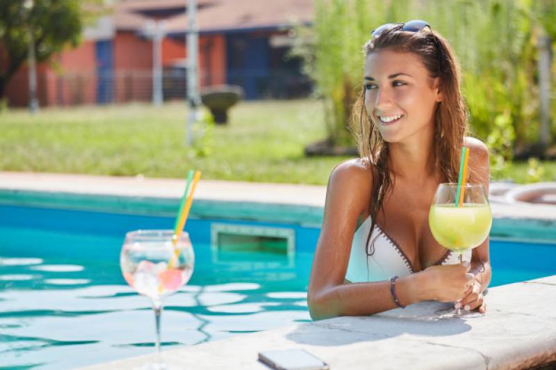 Femme qui boit un cocktail dans sa piscine
